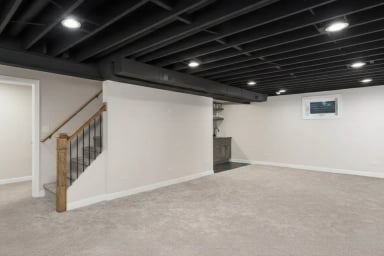 Modern empty basement interior with gray carpet and black ceiling